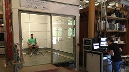 individual sitting alone in a lab room while a person takes notes on a computer